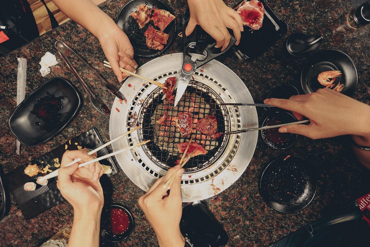 几双手用筷子和夹子在桌上烤炉边烤肉